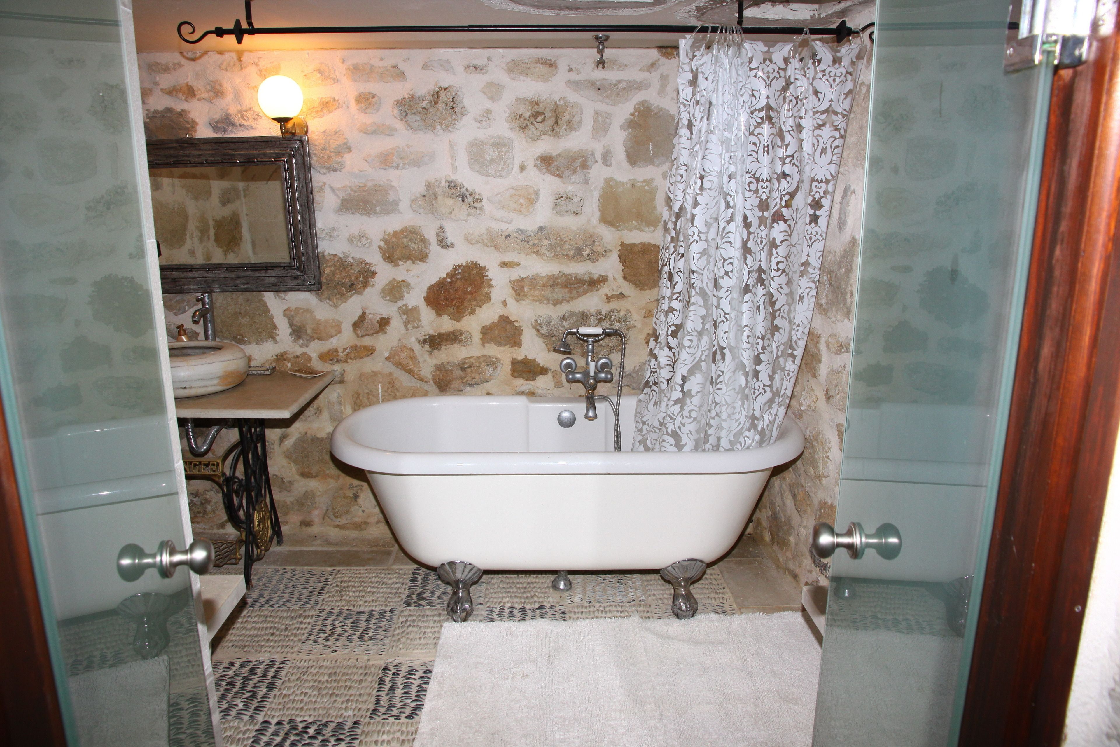 Un baño con pared de piedra, una bañera antigua de patas de león, un lavabo y un espejo.