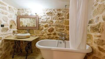 A bathroom with a stone wall, a sink, a mirror, and a bathtub.