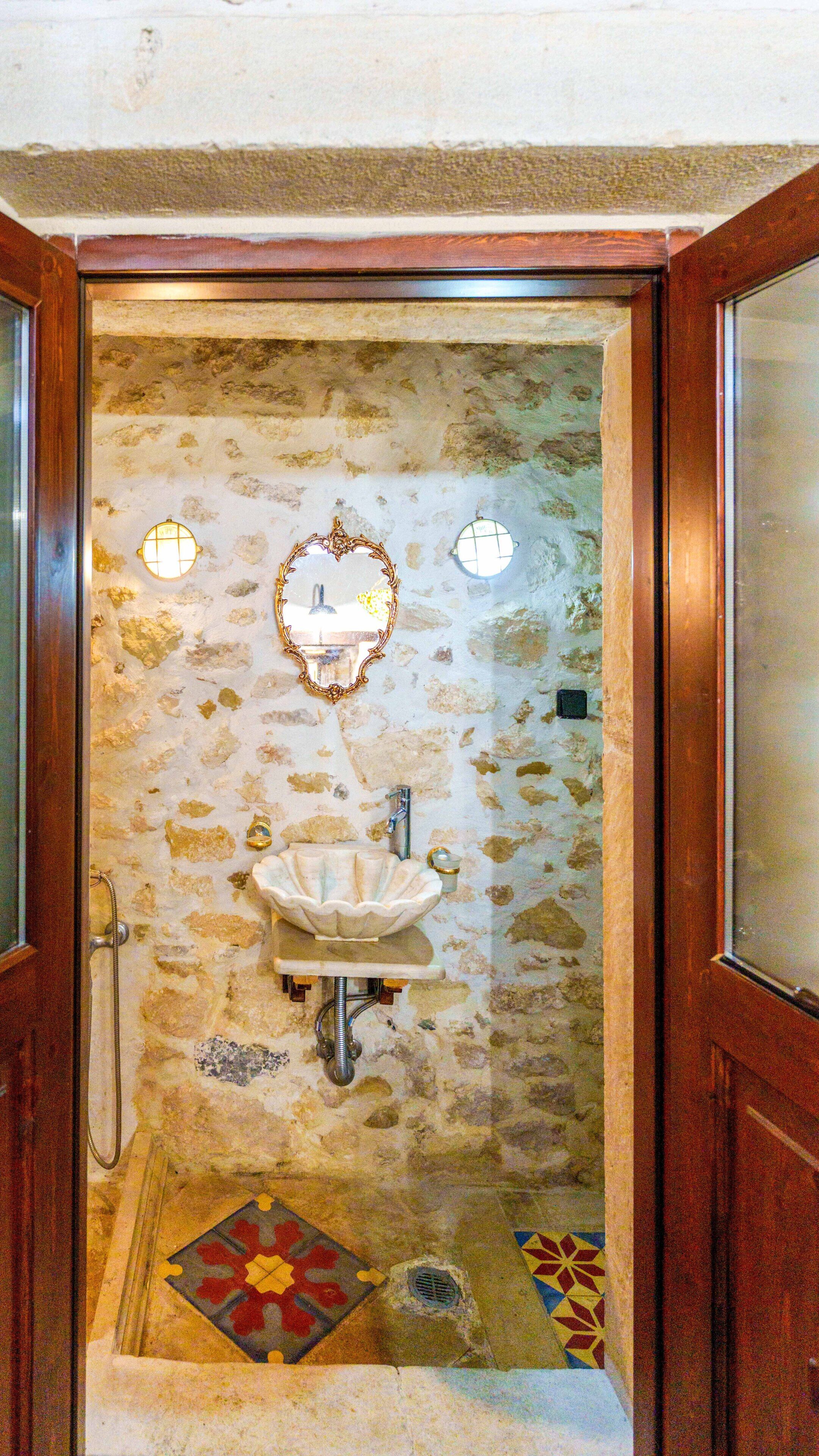 A stone-walled bathroom with a white sink, a mirror, and two wall sconces.