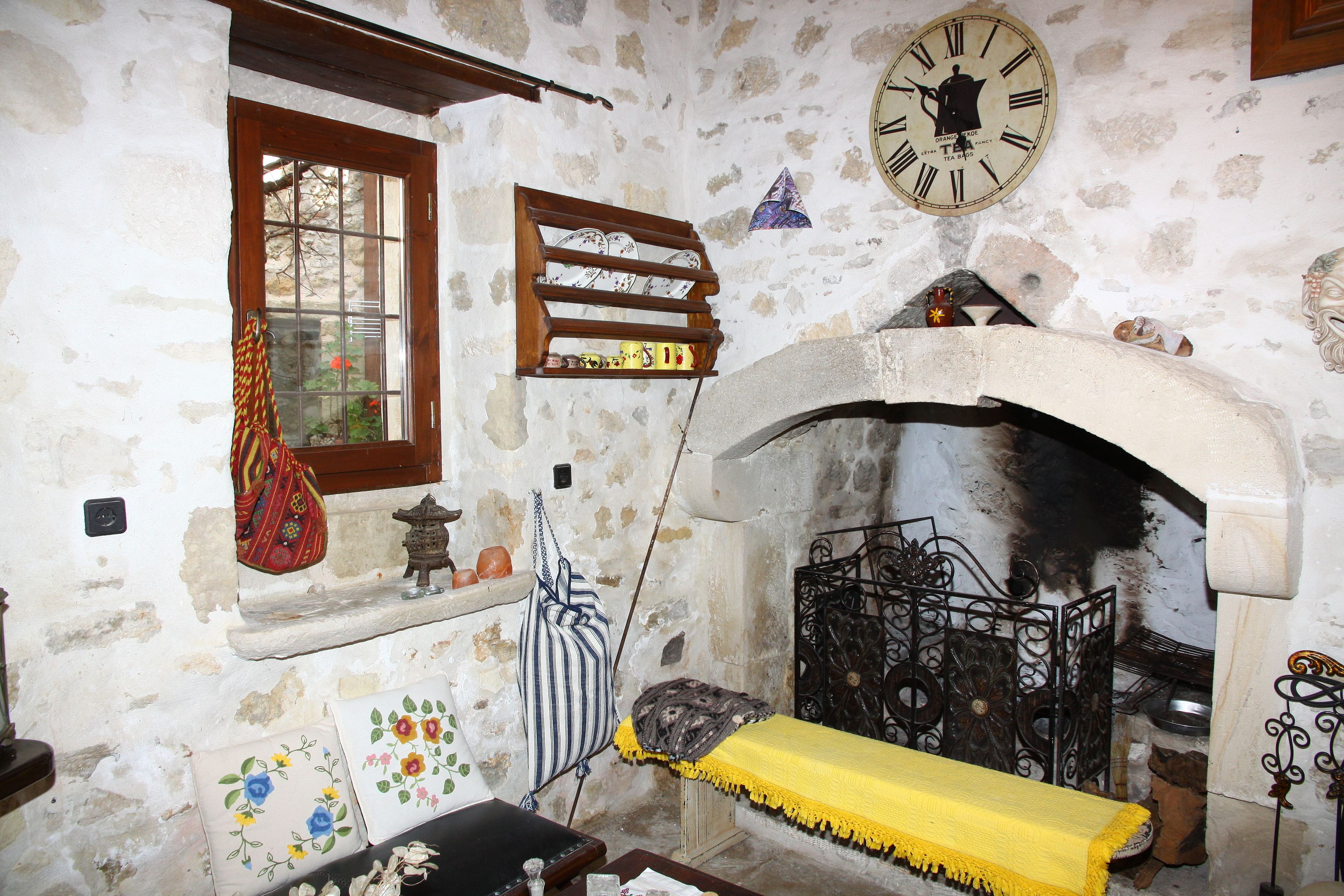 A rustic room with a stone wall, a wooden shelf with decorative items, a fireplace, and a clock.