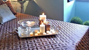 A bedroom with a bed, a bedside table with a lamp, a window with a view, and a tray with candles and a cake. - Torre di Vico Residenza d'Epoca (Viterbo)