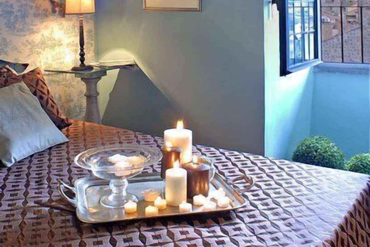Ein Schlafzimmer mit einem Bett, einem Nachttisch mit Lampe, einem Fenster mit Blick und einem Tablett mit Kerzen und Kuchen.