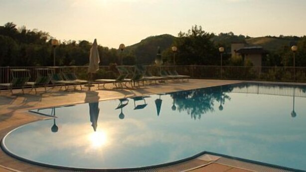A swimming pool with a curved edge, surrounded by lounge chairs and a fence. - Hotel Ducale (Salsomaggiore Terme)