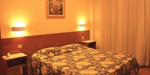 Hotellihuone, jossa on sänky, yöpöydät ja taulu seinällä.