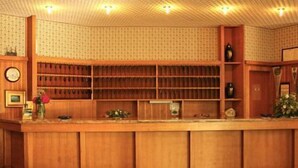A wooden reception desk with a clock, a vase with flowers, and a patterned wall. - Hotel Ducale (Salsomaggiore Terme)