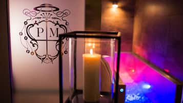 A candle in a glass holder with a logo on the wall behind it.
