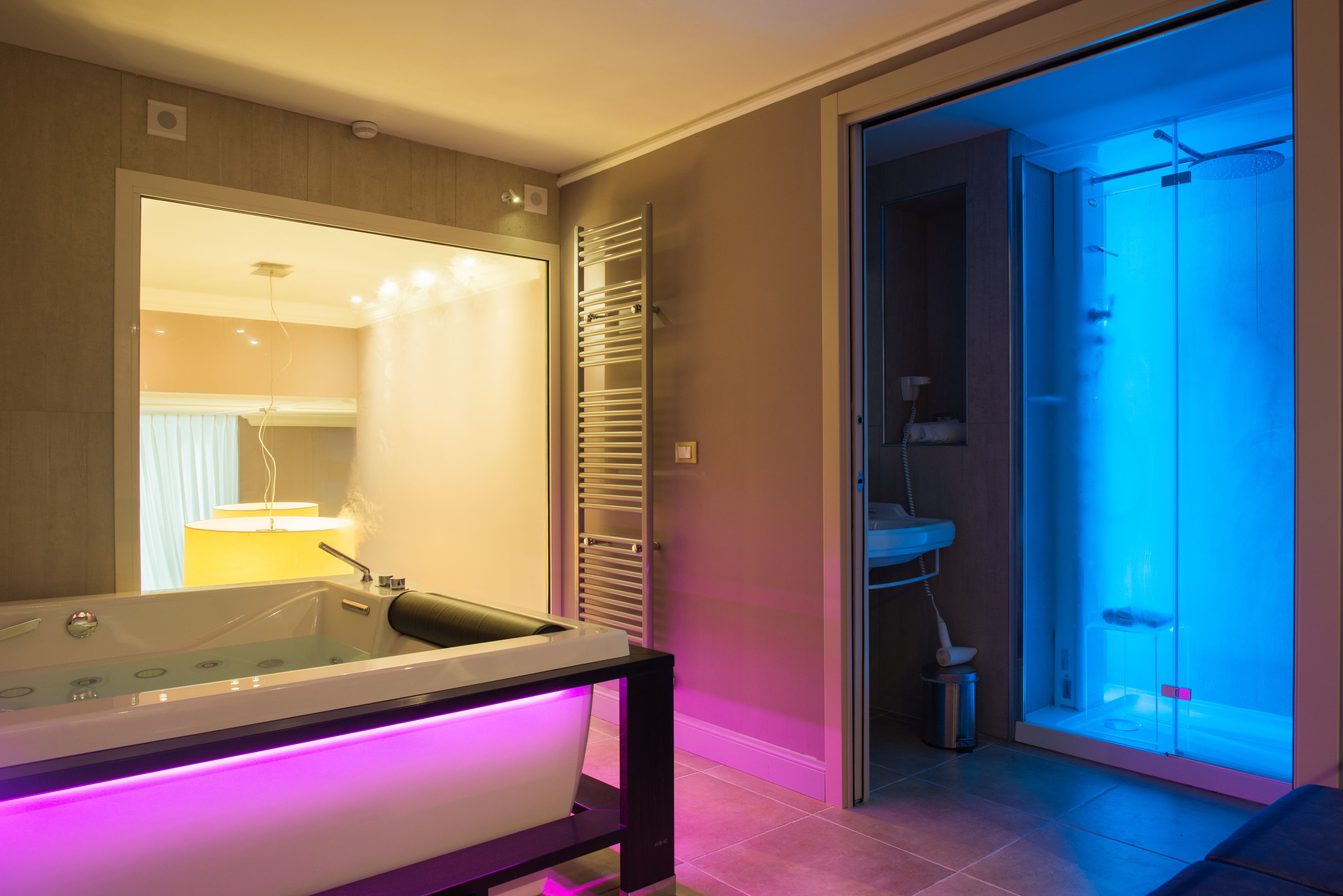 A modern bathroom with a glass-enclosed shower, a standalone bathtub with LED lighting, and a visible towel rack.