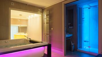A modern bathroom with a glass-enclosed shower, a standalone bathtub with LED lighting, and a visible towel rack.