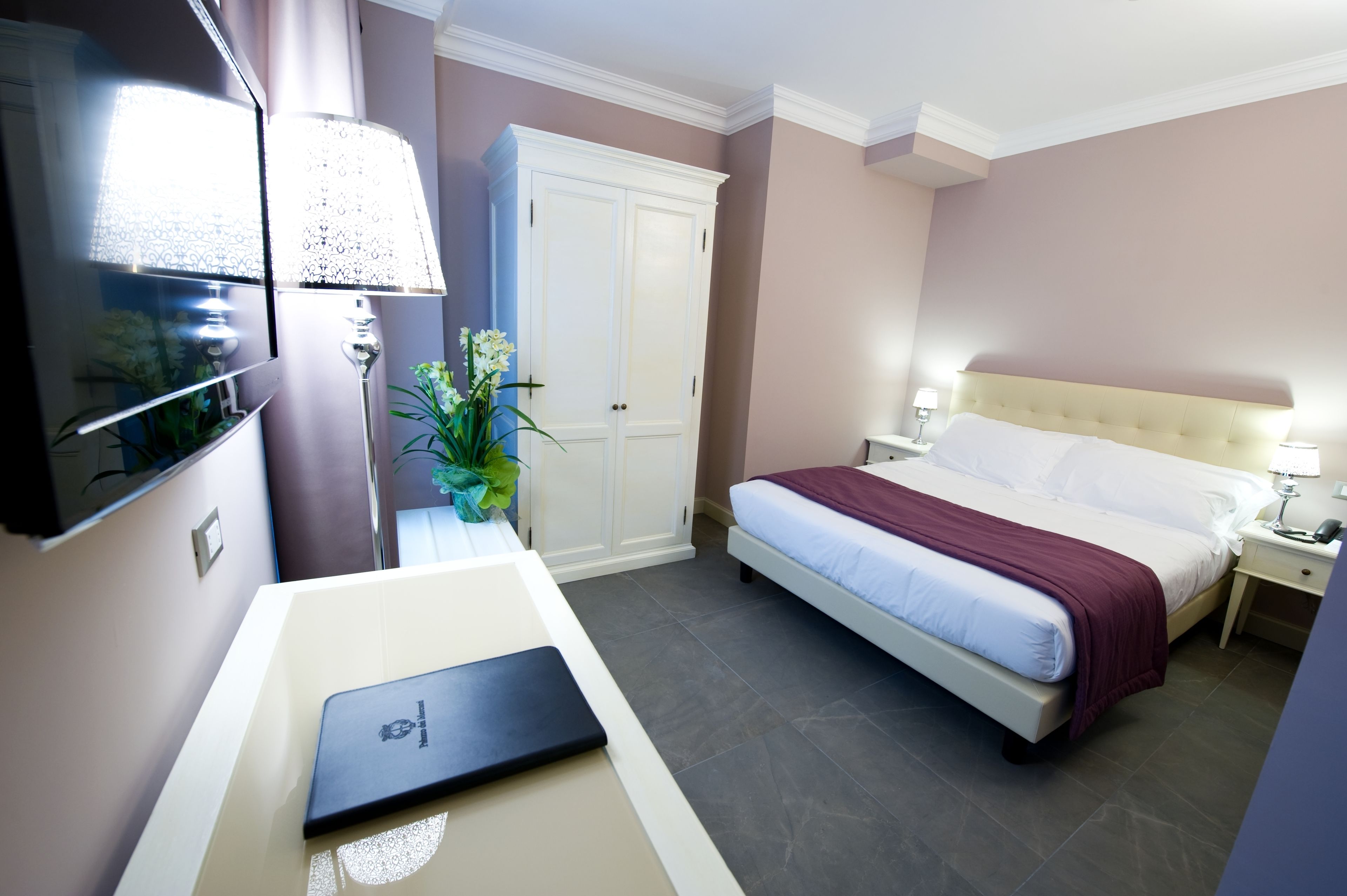 Una habitación de hotel con cama, escritorio, televisión, armario y una planta en maceta.