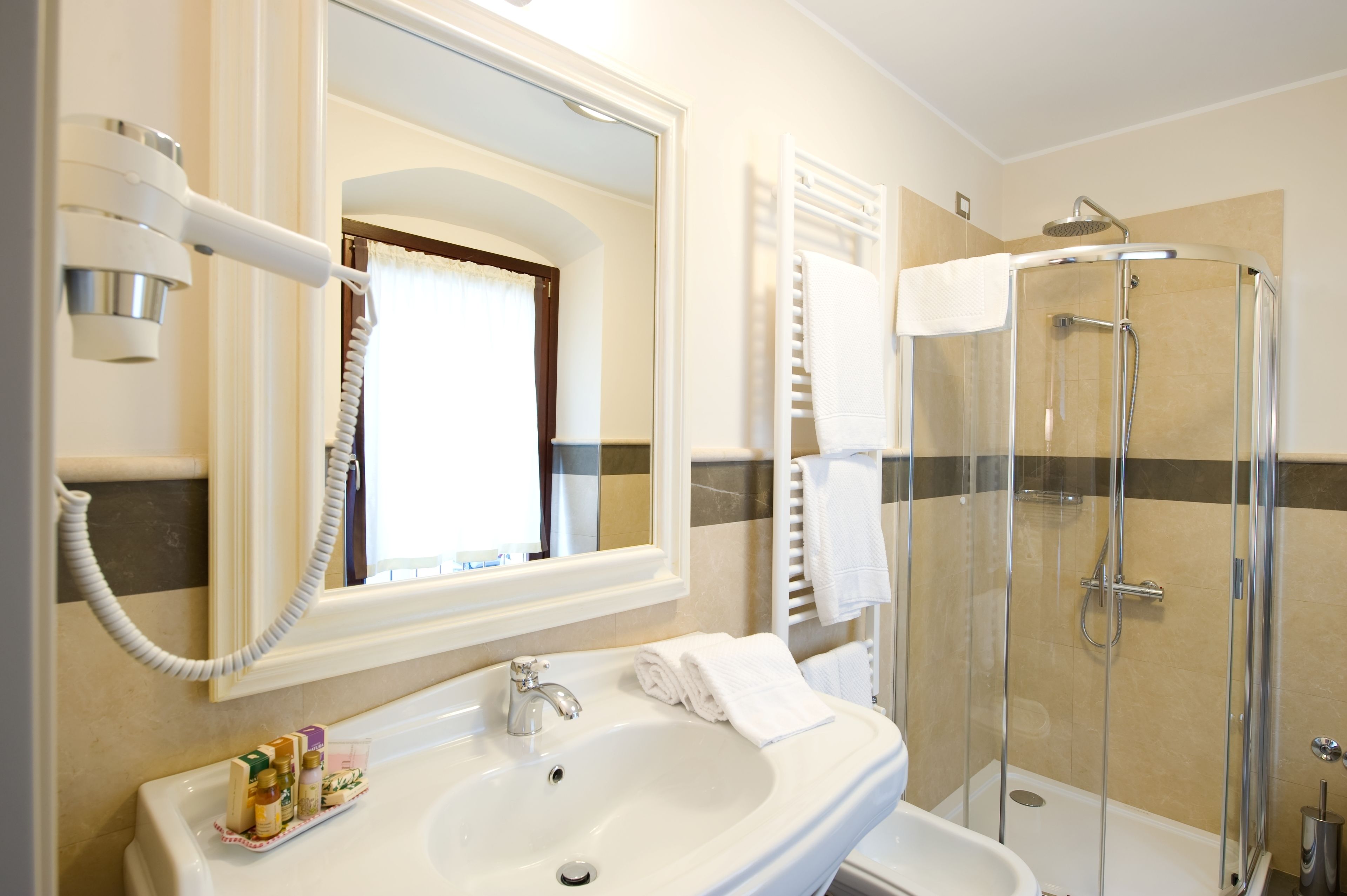 A bathroom with a sink, mirror, hairdryer, and a glass-enclosed shower.