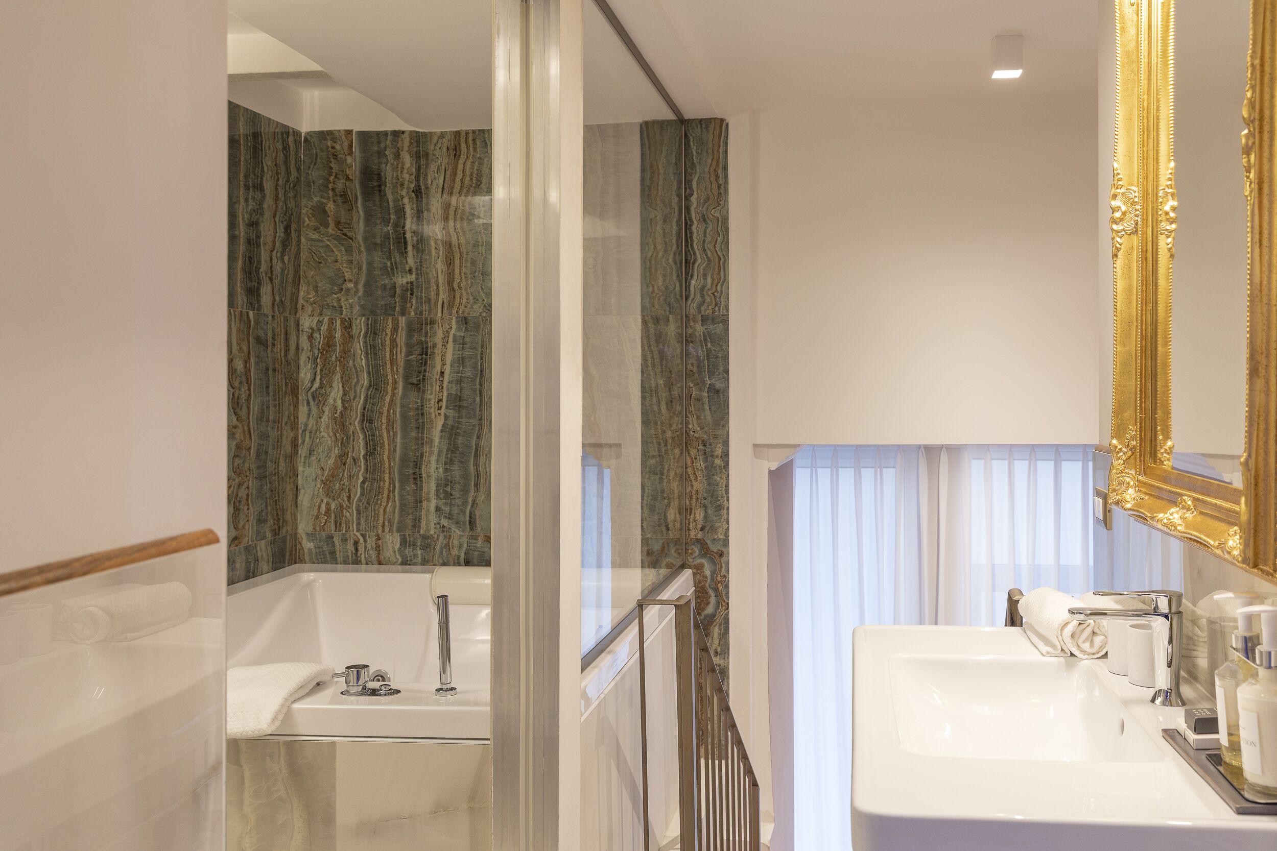 A modern bathroom with a glass-enclosed shower, a white sink, and a large mirror with a gold frame.