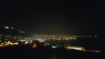 Een nachtelijke stadsgezicht met uitzicht op water en een lichtgevende heuvel.