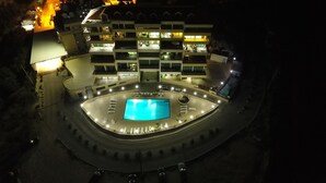 Un hôtel à plusieurs étages doté d’une piscine centrale, d’un espace extérieur aménagé et d’une façade bien éclairée.