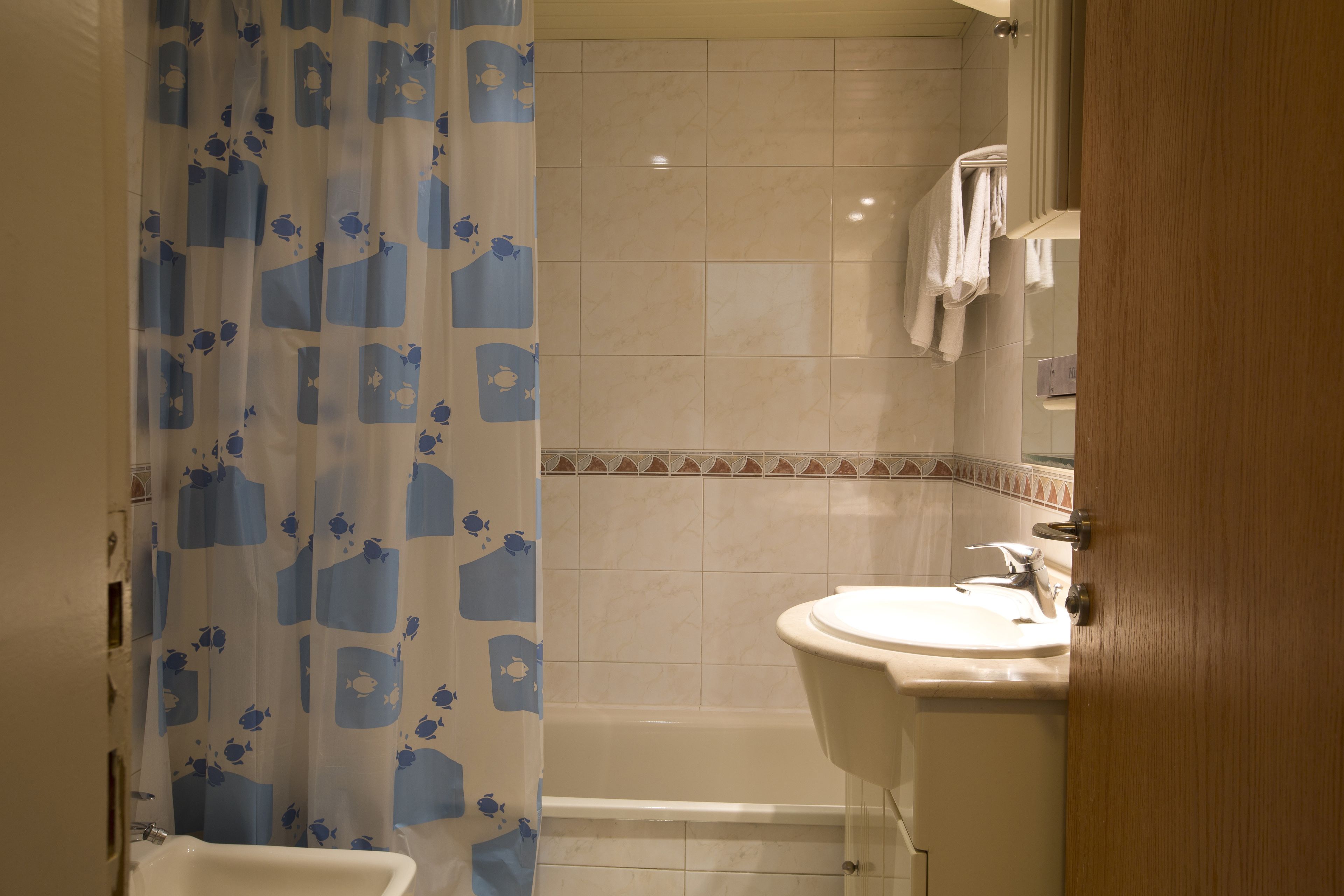 A bathroom with a shower curtain, a bathtub, a sink, and a mirror.