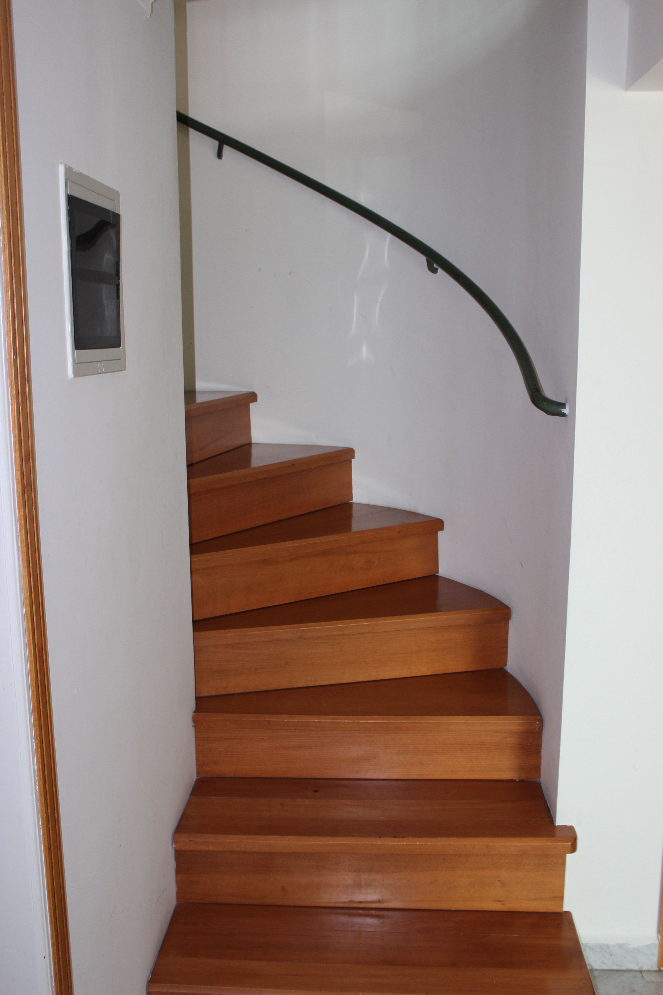 A wooden staircase with a black handrail leading to an upper floor.