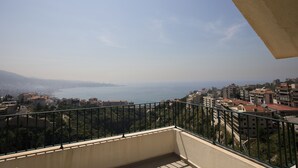 Un balcon offrant une vue sur un paysage urbain côtier, avec des bâtiments et une étendue d’eau.