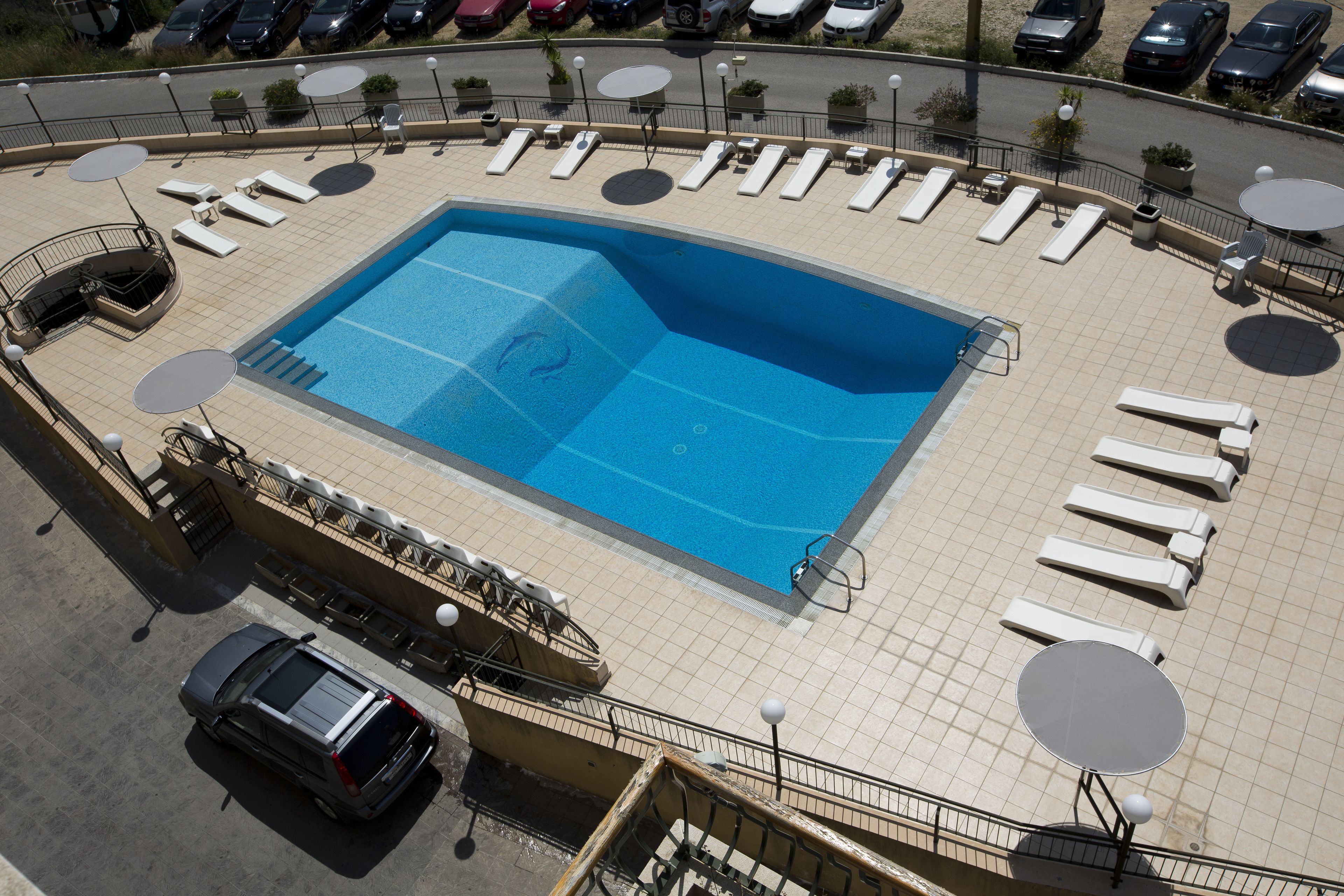 A rooftop swimming pool with sun loungers and a car parked nearby.