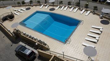A rooftop swimming pool with sun loungers and a car parked nearby.