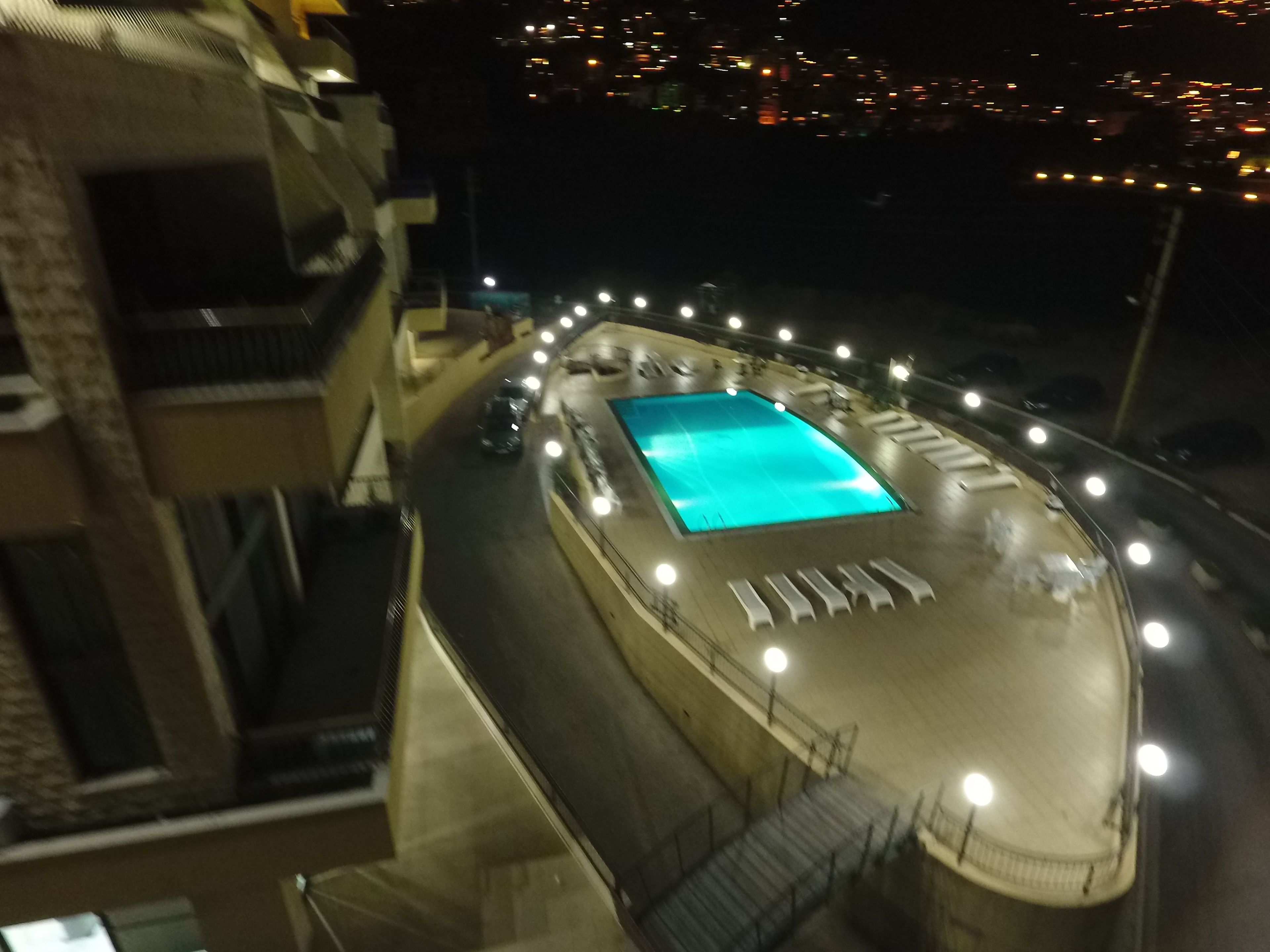 Una piscina de forma rectangular, rodeada por un muro bajo y una serie de luces.