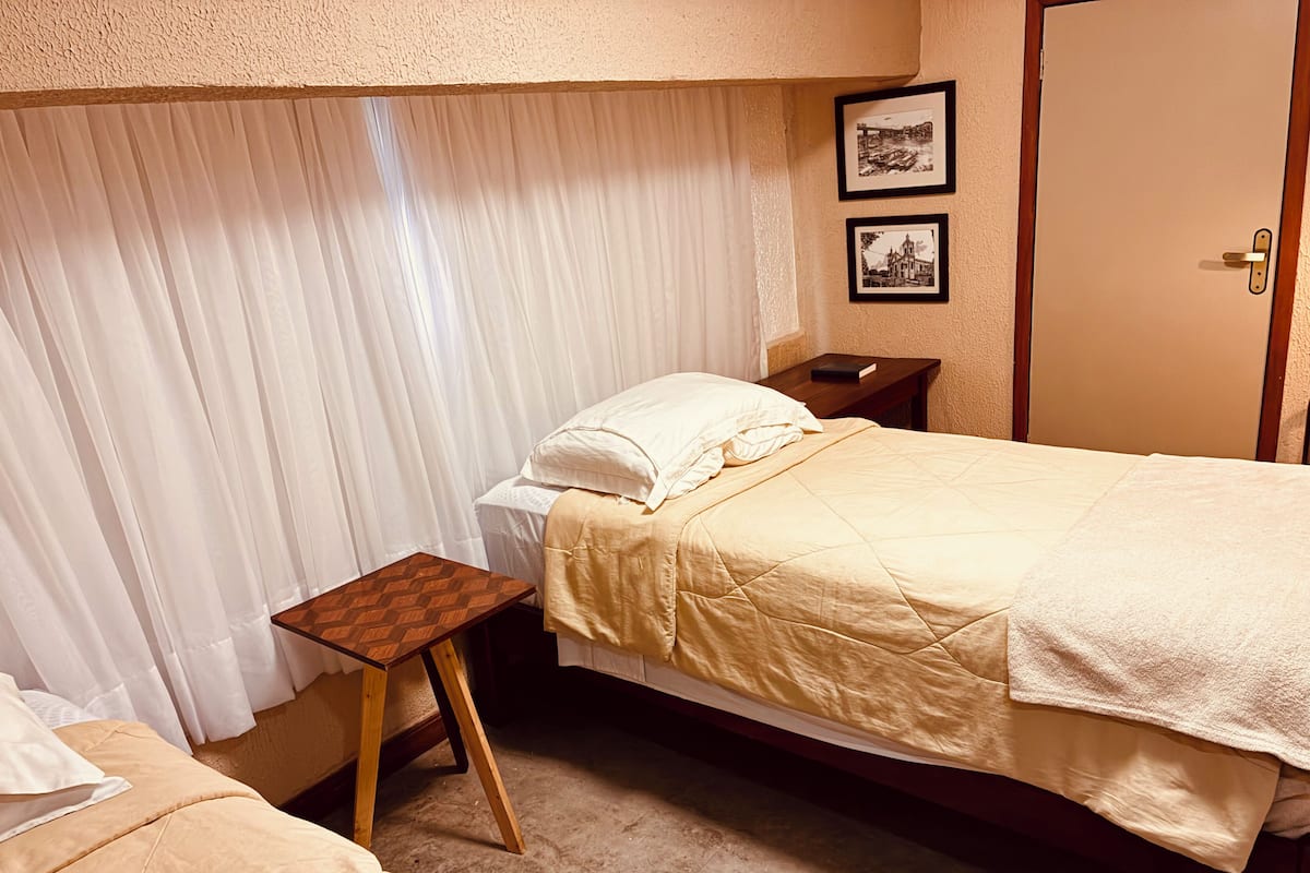 A bedroom with a bed, a small wooden table, a nightstand, and two framed pictures on the wall.