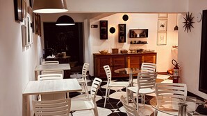 Un comedor con sillas y mesas blancas, piso de baldosas blanco y negro, y un mueble de madera con objetos decorativos.