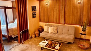Una habitación con sofá, una mesa de centro con un juego de mesa, una cama con cortinas y una pared con persianas verticales.
