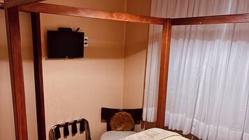 Un dormitorio con cama, televisor en la pared, una silla y una ventana con cortinas.