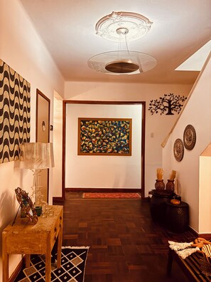 A hallway with a wooden floor, a framed painting, a lamp, and a decorative tree on the wall.