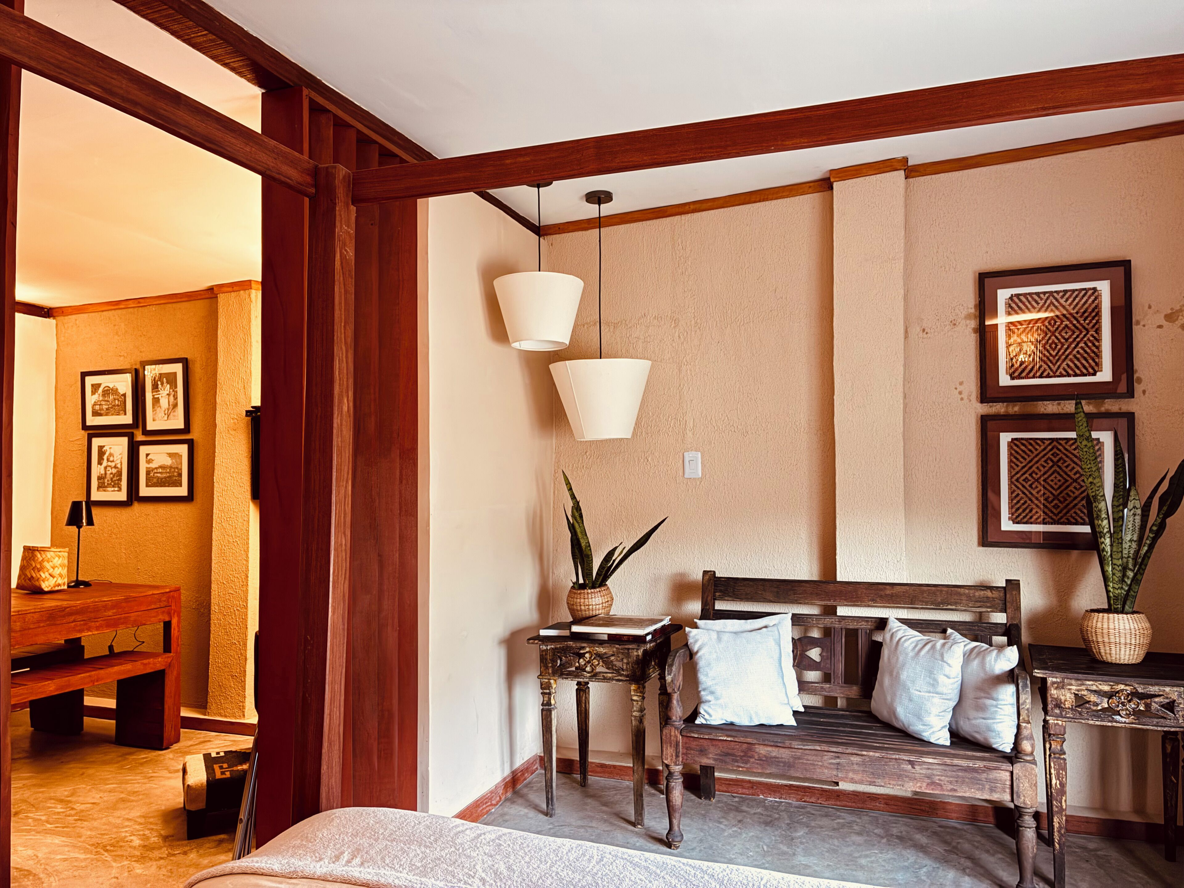 Una habitación con un banco de madera, una pequeña mesa con una planta y cuadros en la pared.