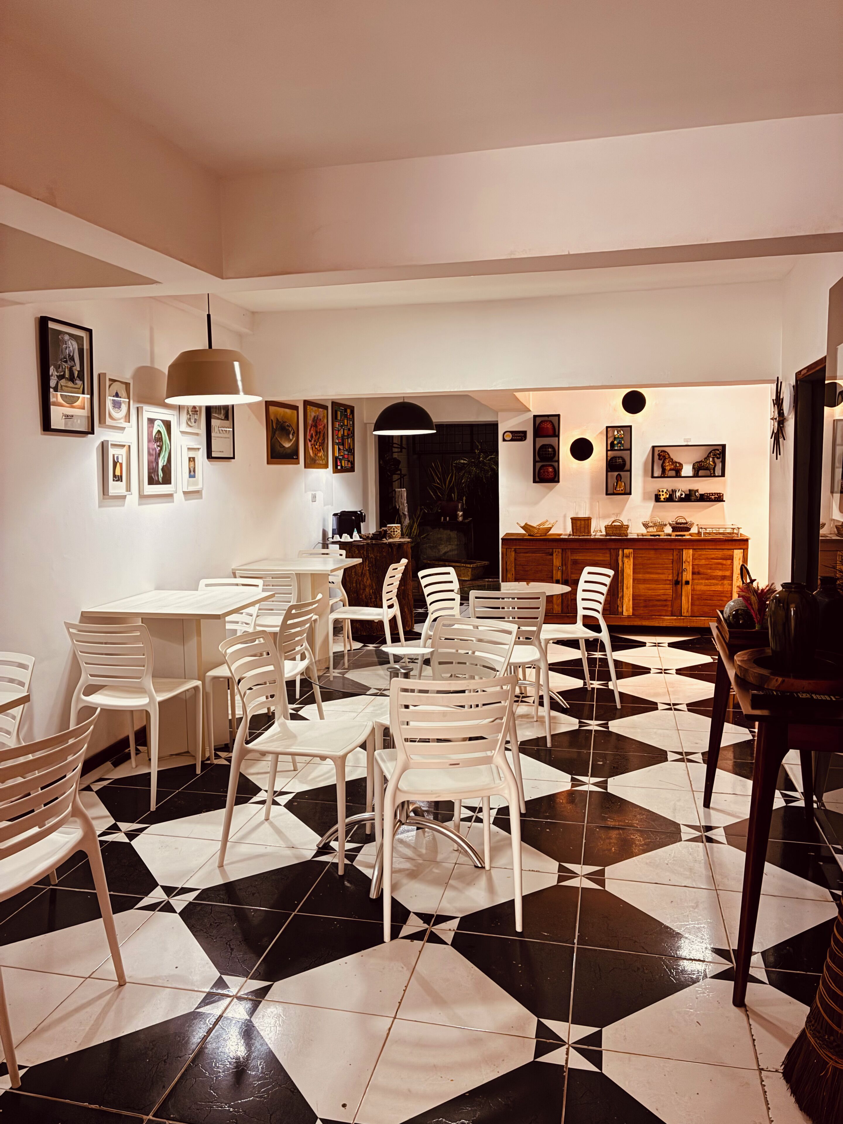 Un comedor con sillas blancas, piso de baldosas blanco y negro, y un mueble de madera con cestas.