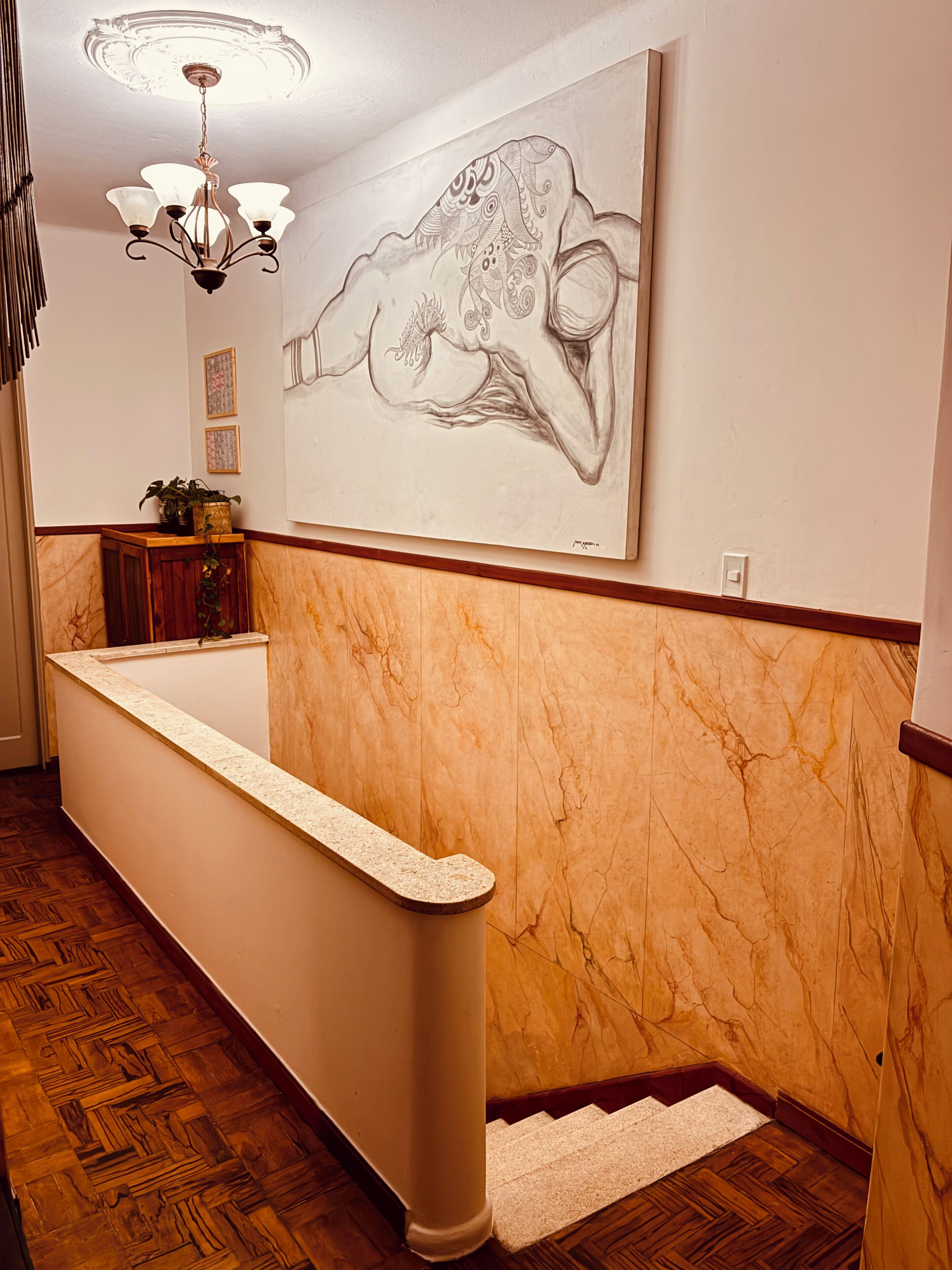 Un área de recepción con pared de mármol, mostrador de recepción, una araña de cristal y un cuadro mural grande.