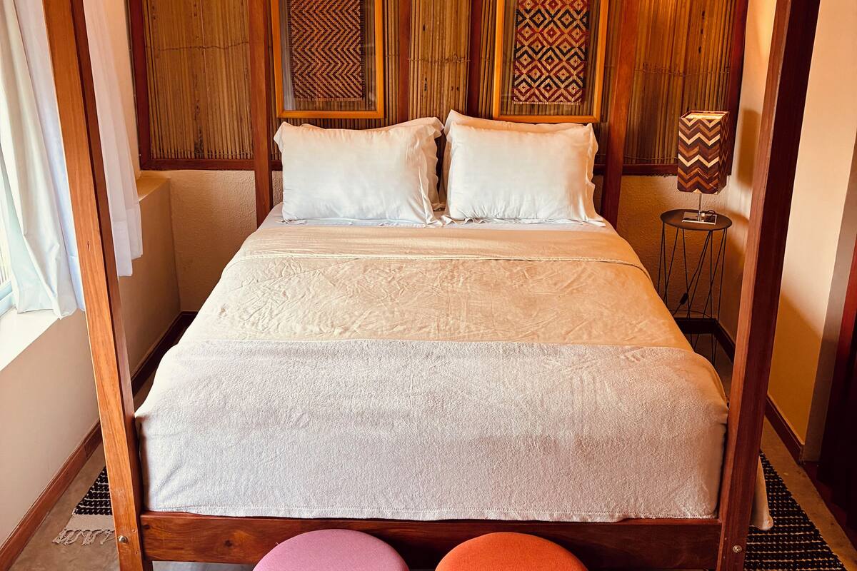 A four-poster bed with a wooden frame, two pillows, and a patterned headboard.