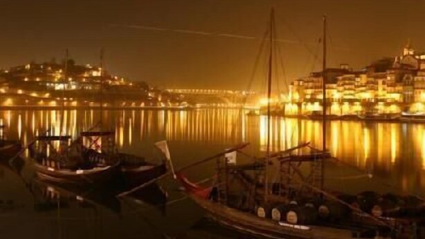 Cena noturna à beira-mar, com barcos atracados perto de edifícios com iluminação acolhedora.