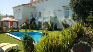 Um edifício grande e branco com piscina, área de estar externa e vegetação exuberante.