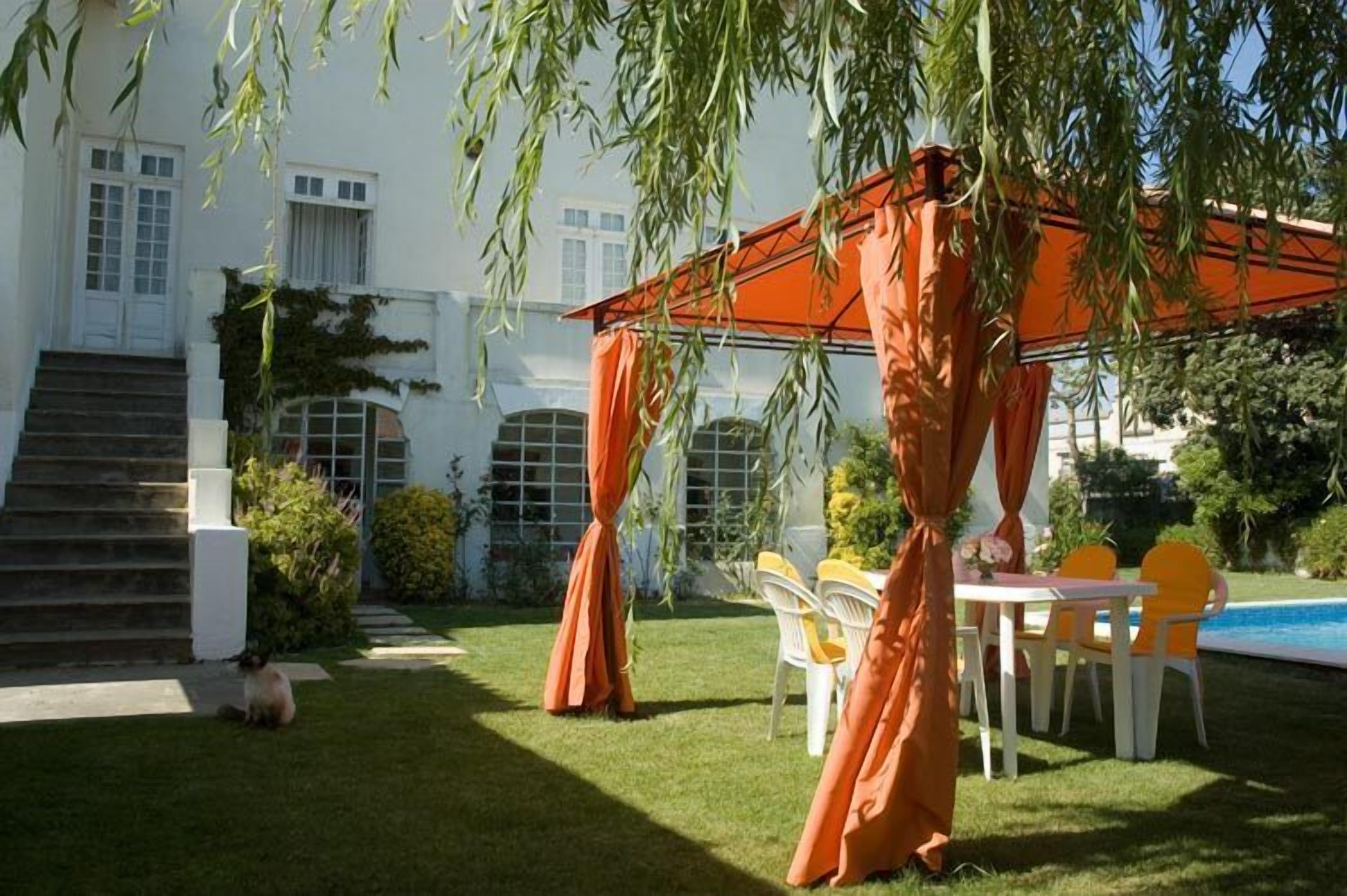 Un jardín con un edificio blanco, una piscina y cortinas naranjas.