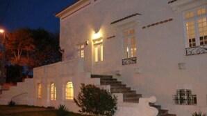 Um edifício branco com uma escadaria que leva à entrada, grandes janelas e fachada bem iluminada.