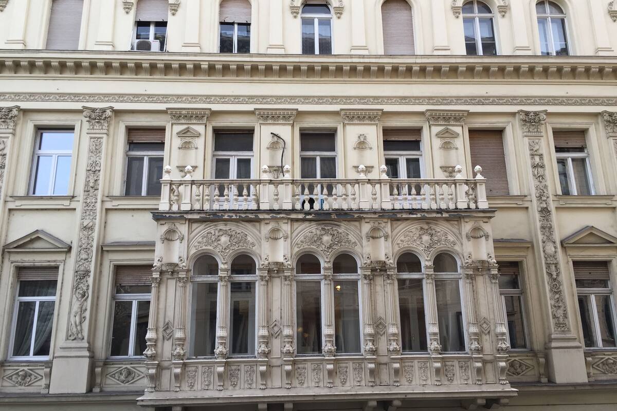 Un edificio con detalles arquitectónicos ornamentados, incluyendo un balcón con barandillas decorativas y varios ventanales de arco.