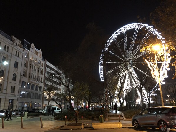 A nighttime city street with a large Ferris wheel, buildings, and parked cars.