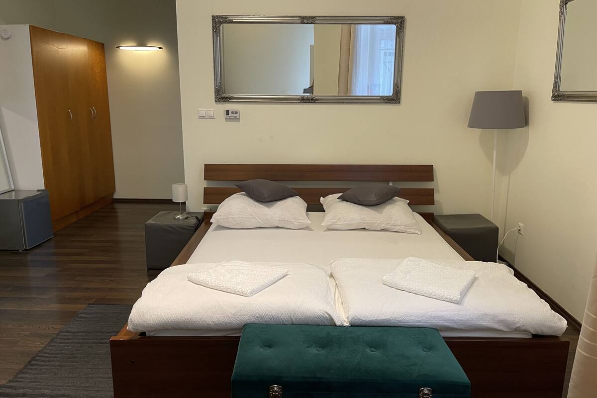 Habitación de hotel con una cama grande, dos mesitas de noche, un taburete verde, un espejo y un armario.