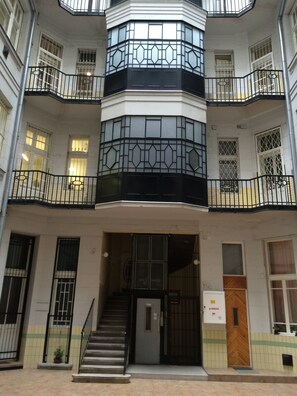 A multi-story building with a central atrium, balconies, and a staircase leading to the entrance.