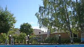 Une piscine à l’eau d’un bleu cristallin, entourée d’arbres, avec un bâtiment visible au loin.