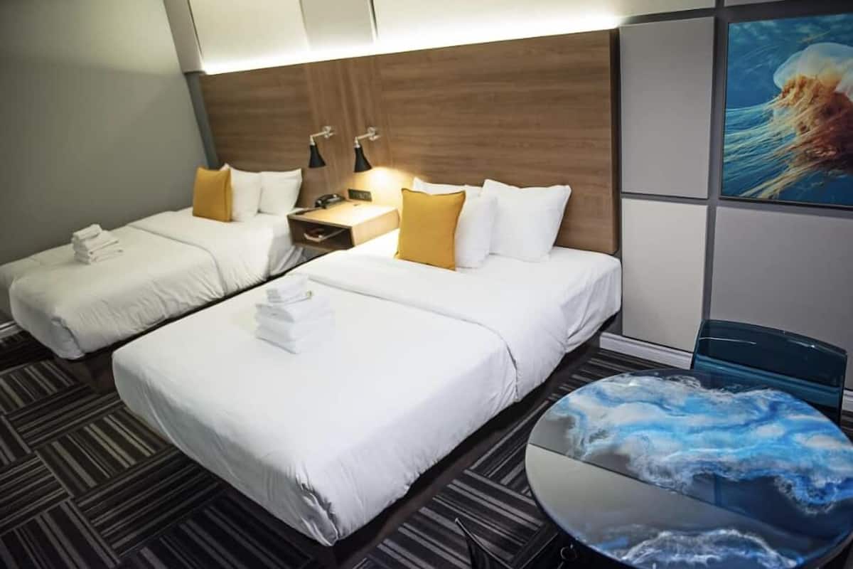 Une chambre d’hôtel avec deux lits, une table ronde au motif évoquant le marbre et un tableau représentant une méduse accroché au mur.