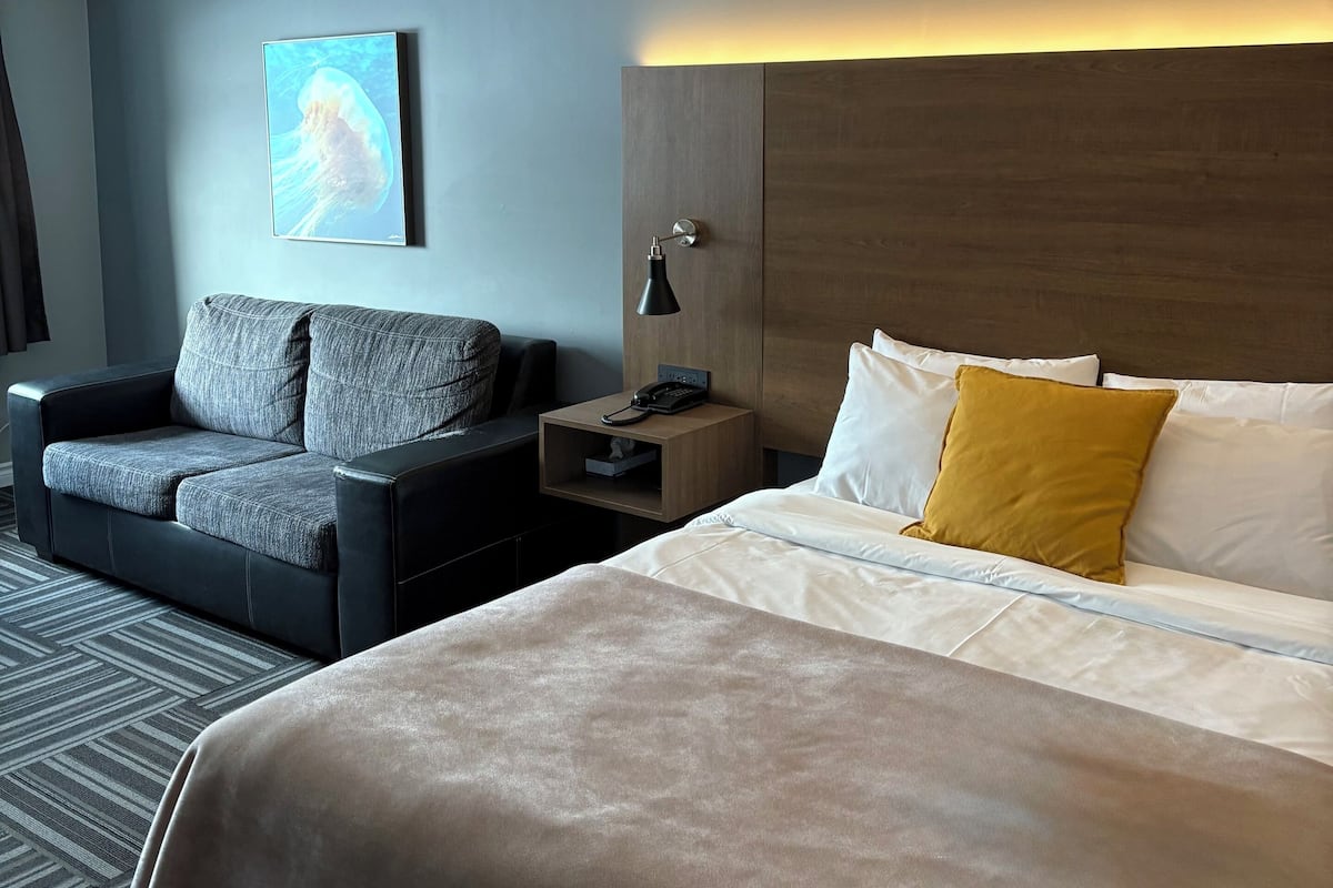 Une chambre d’hôtel avec un grand lit, un canapé, une table de chevet avec une lampe et un tableau accroché au mur.