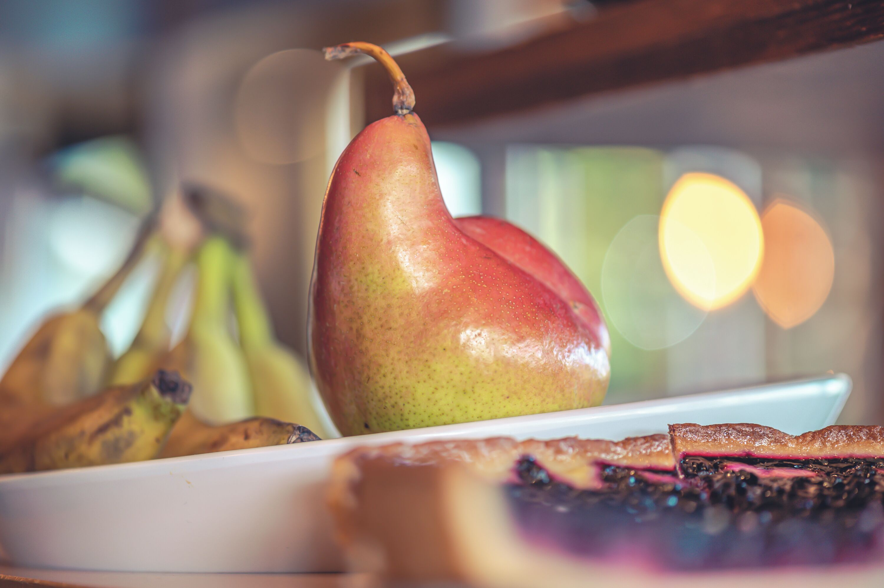 A pear on a plate with bananas and a slice of cake.