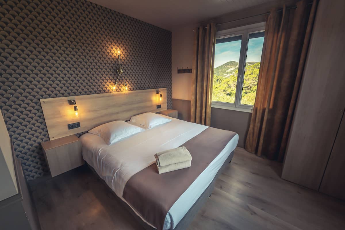 A neatly made bed with a wooden headboard, a nightstand, and a window with curtains.