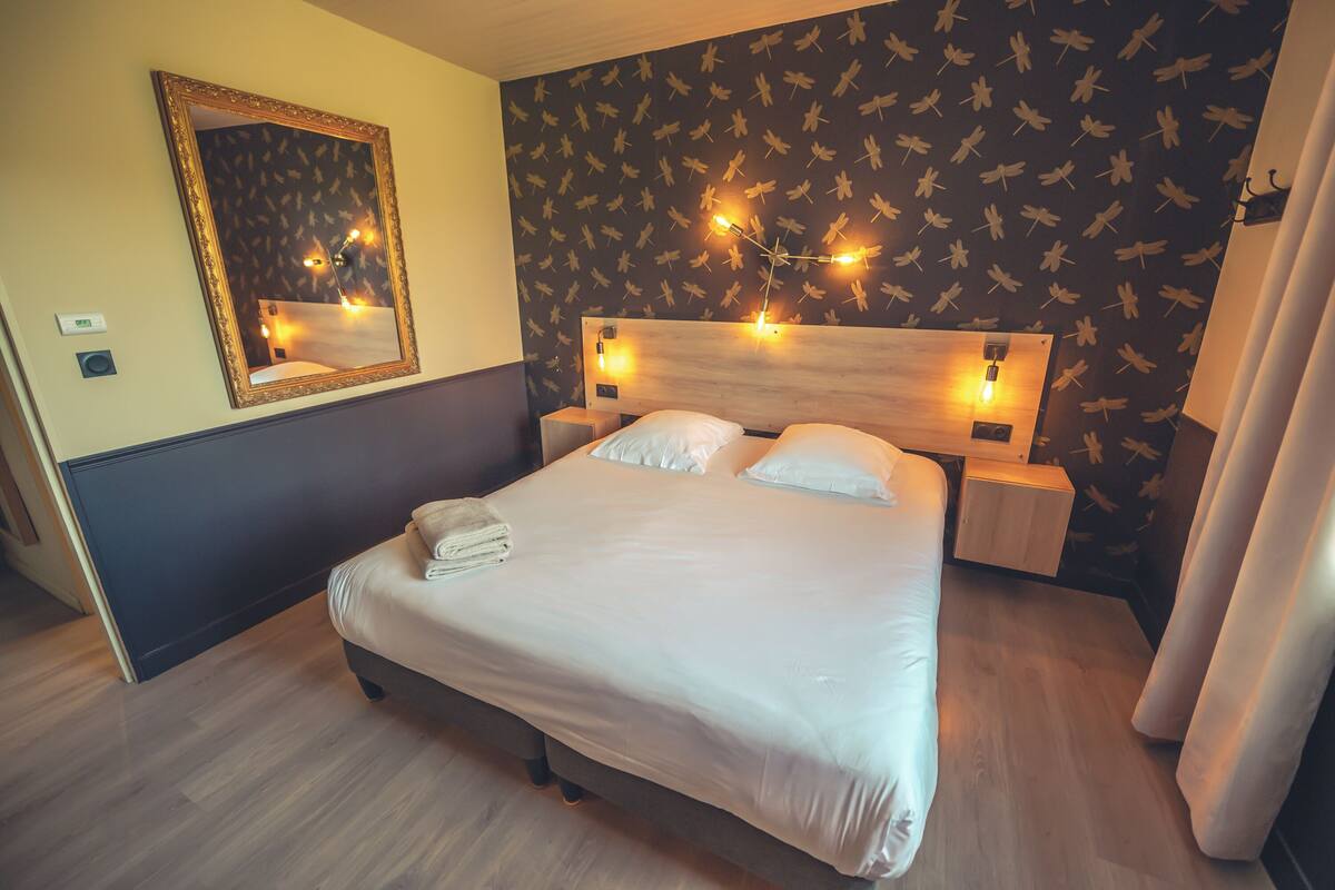 A neatly made bed with a wooden headboard, two bedside tables with lamps, a mirror, and a wall with a bird pattern.