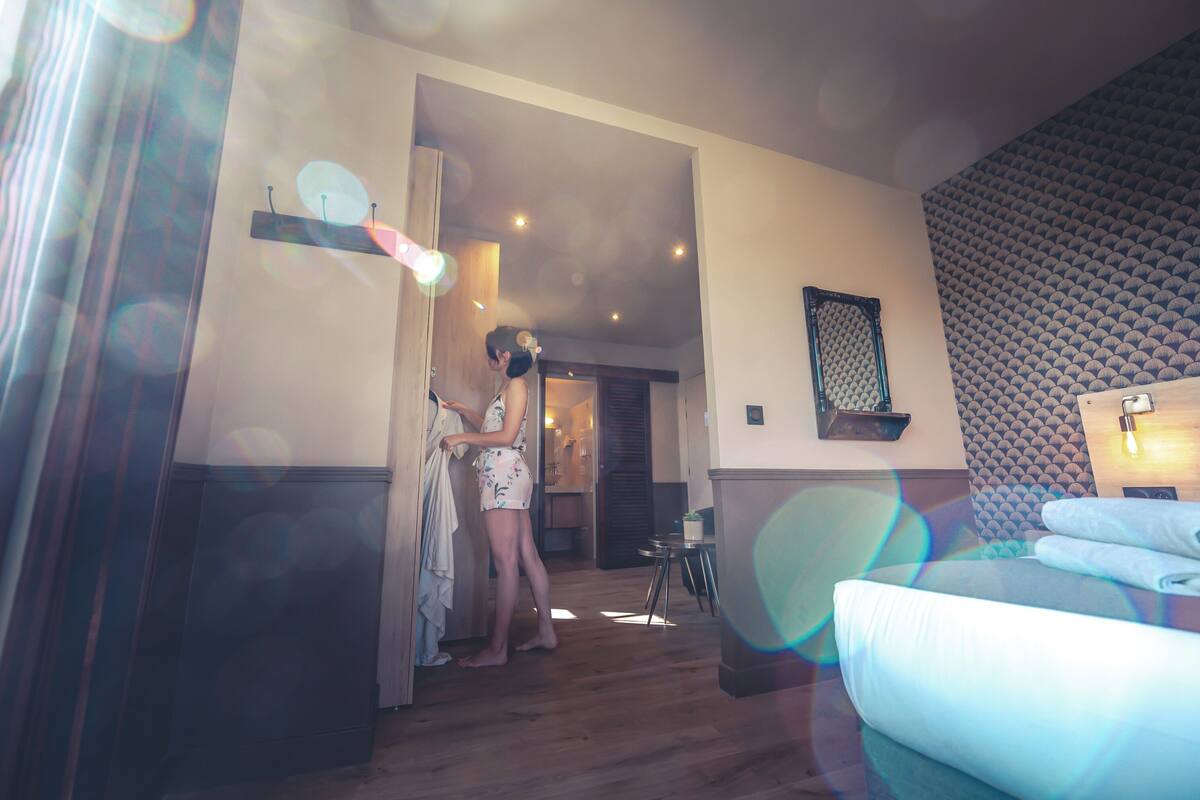 A hotel room with a bed, a small table, and a wall-mounted shelf.