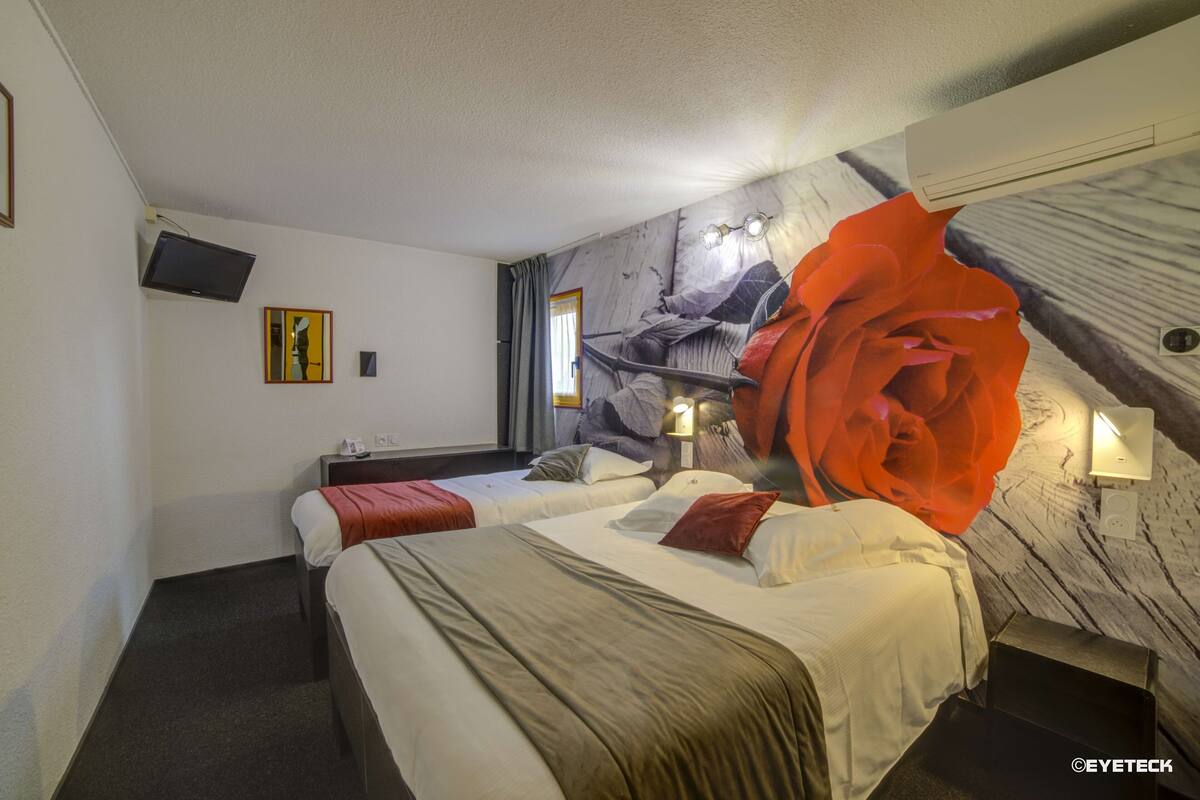 A hotel room with two beds, a large wall mural, a mounted television, and a window with curtains.