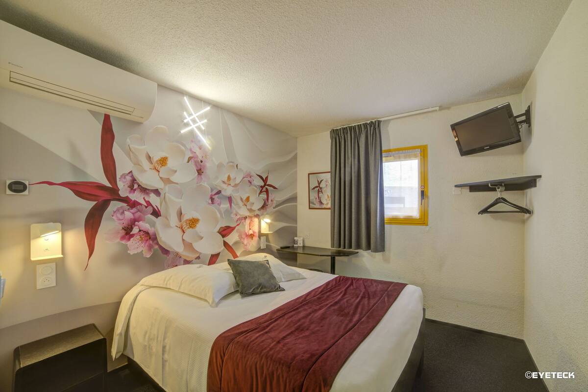 A hotel room with a bed, a flat-screen TV, a wall-mounted TV, a painting, and a window with curtains.