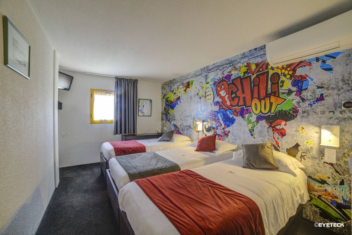A hotel room with three beds, a large graffiti wall, and a window with curtains.